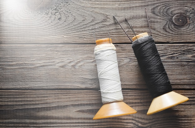 White and black coils of thread with needles on rustic wooden.