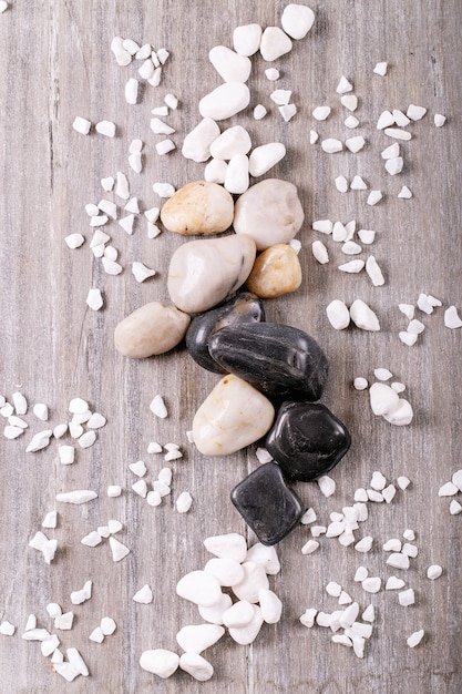 White, black decorative rocks and pebbles over grey wooden background. Top view, flat lay. Copy space