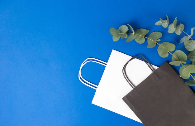 White and black paper bags with handles and eucalyptus leaves on blue background. flat lay banner, top view, copy space, zero waste, plastic free items. mockup eco package