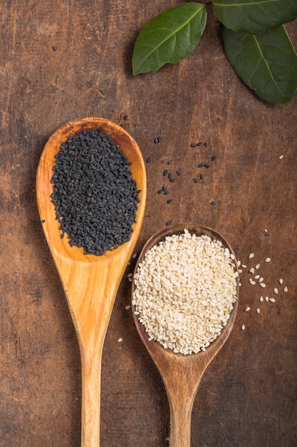 White and black sesame seeds in spoons on wooden table