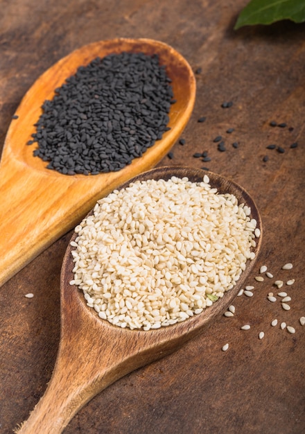 White and black sesame seeds in spoons on wooden table