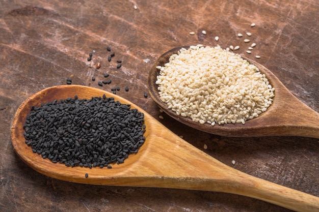 White and black sesame seeds in spoons on wooden table