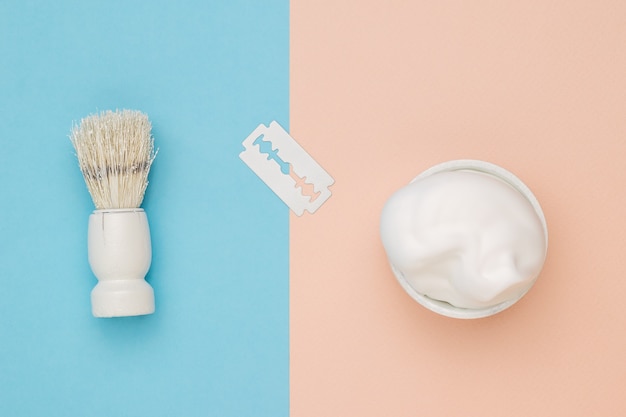 White blade, foam and shaving brush on beige and blue background.