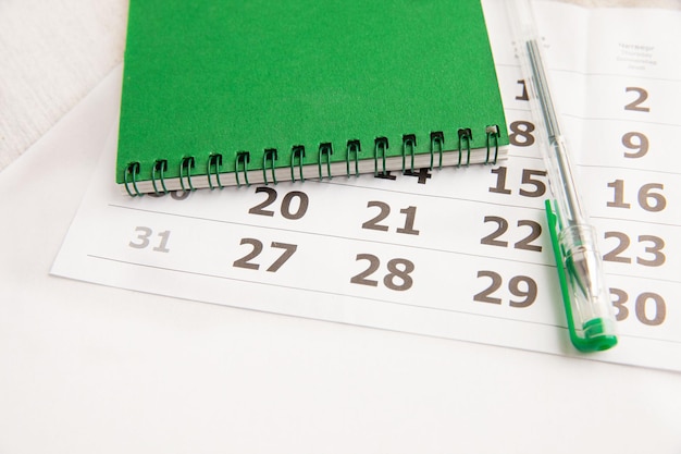 White blank calendar with notepad, with green pen on white\
background, work planning concept.