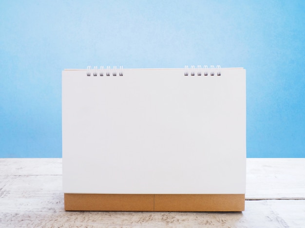 White blank calendar on wooden vintage table over blue cement wall