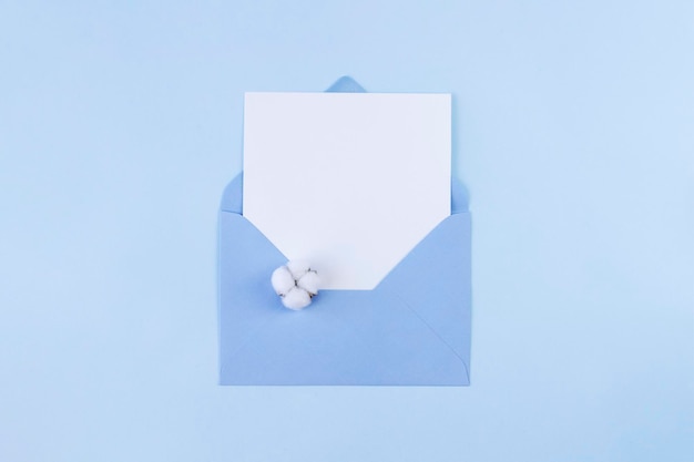 White blank card in blue envelope with one cotton flower on blue background