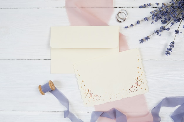 White blank card, envelope and ribbon with two wedding rings on pink fabric 