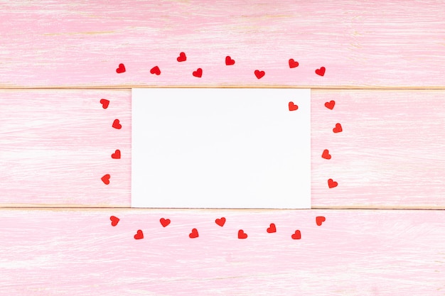 写真 ピンクの木製の背景に赤い紙吹雪心と白い空白カード