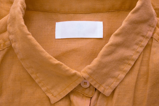 Foto etichetta dell'etichetta dell'abbigliamento in bianco bianca sul fondo di struttura del tessuto della camicia di lino marrone