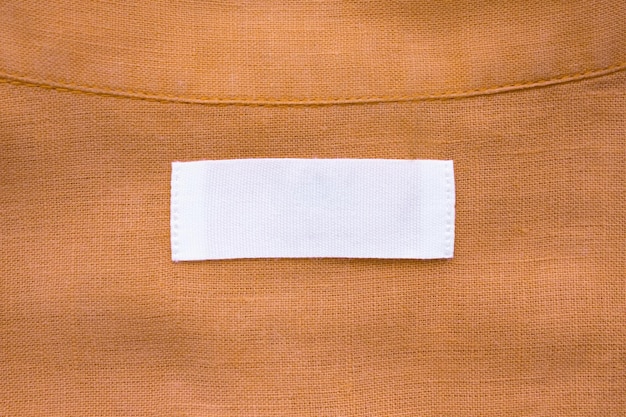 Photo white blank clothing tag label on brown linen shirt fabric texture background
