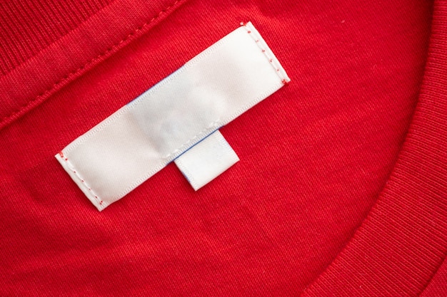 White blank clothing tag label on new red cotton shirt fabric texture background