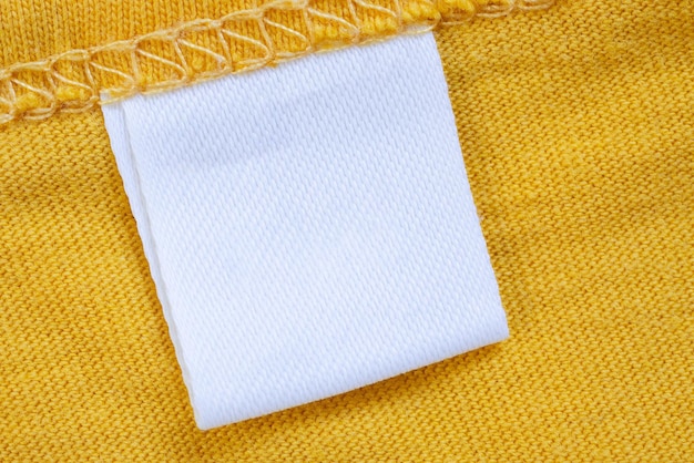 White blank clothing tag label on new yellow shirt background