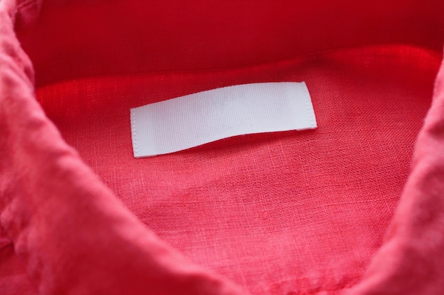 White blank clothing tag label on red linen shirt fabric texture background