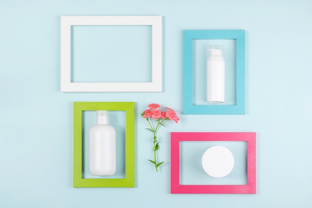 White blank cosmetic bottle, tube, jar, one flower and bright frames on blue