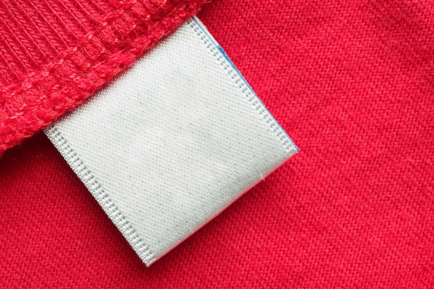 Белая пустая этикетка для стирки одежды на фоне красной хлопковой рубашки
