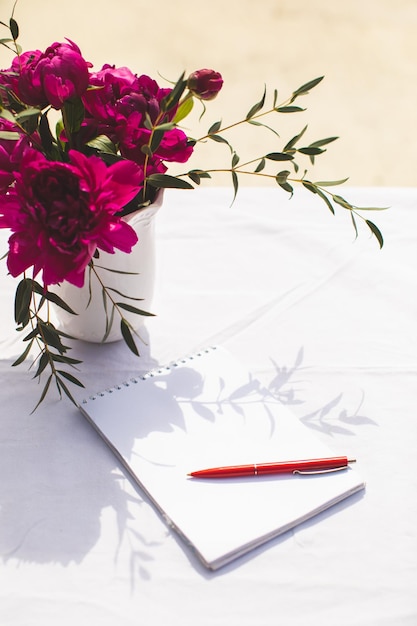 Photo white blank note book with red pen and purple bouquet of peony flowers on white tablecloth planning or diary writing concept