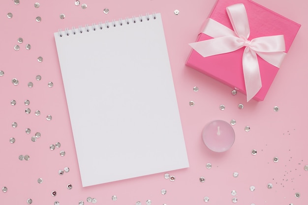 White blank notepad sheet, pink candle, gift box and confetti on pink wall, Happy Valentine's Day