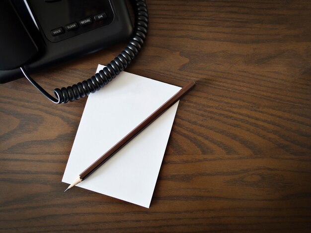 Photo white blank paper, pencil, and telephone on brown wooden table