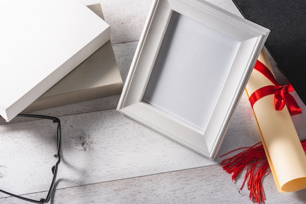 White blank photo frame and education or graduation equipment on wooden white table