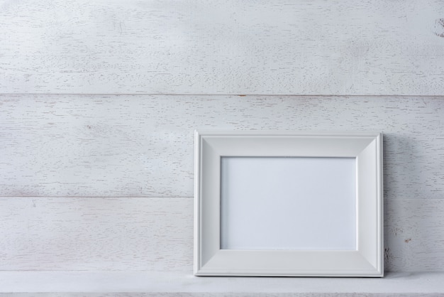 White blank photo frame on wooden shelf and wall