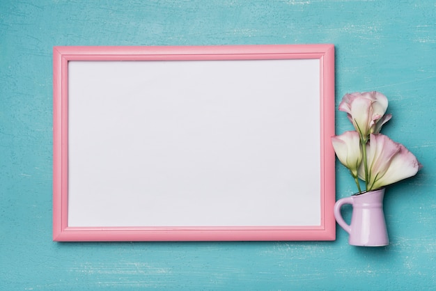 Photo white blank picture frame with pink border and vase on blue background