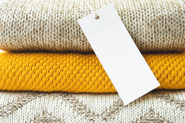 White blank rectangular clothing tag on stack of knitted clothes background close up