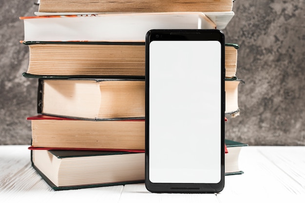 Foto telefono mobile bianco della visualizzazione dello schermo in bianco davanti al libro impilato sulla tavola