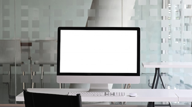 Foto monitor bianco dello schermo in bianco che mette sullo scrittorio funzionante bianco con il topo e la tastiera senza fili sopra l'ufficio moderno.
