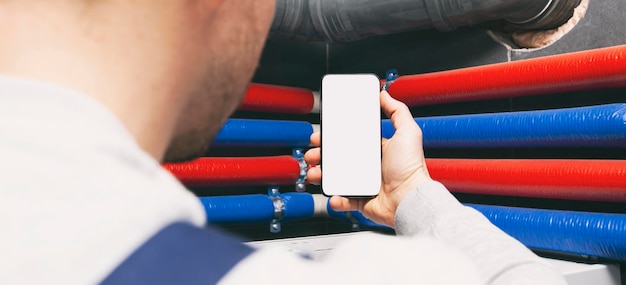 Foto schermo bianco vuoto sul telefono in mano all'idraulico nel mockup di guanti di protezione per la riparazione della casa o la costruzione o l'installazione di un sistema di riscaldamento