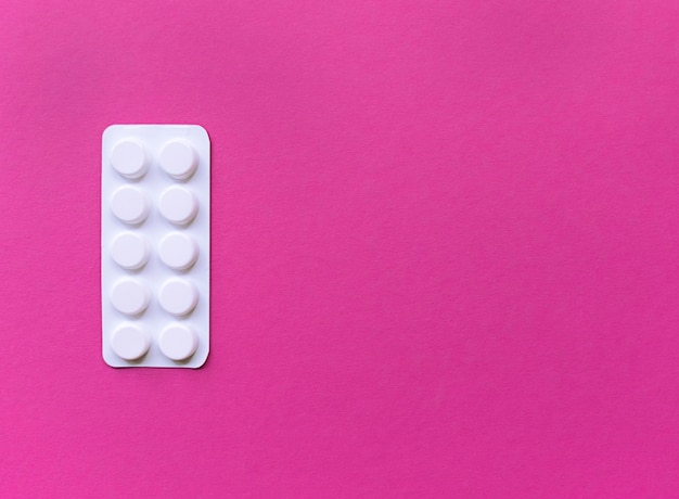 White blister of pills on pink background. Simple flat lay with pastel texture with copy space. Medical concept. 