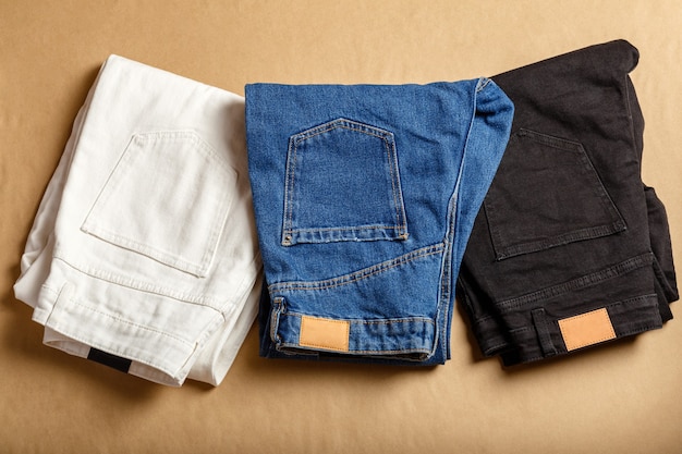 Pantaloni jeans neri blu bianchi impilati. assortimento di abbigliamento in denim di colore diverso nel negozio del negozio. pantaloni jeans in denim bianco, blue jeans, denim nero. vista dall'alto sul tavolo marrone.