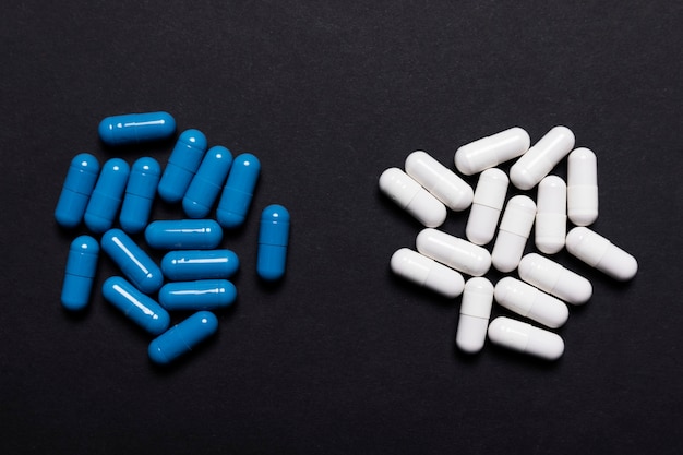 White and blue capsule pills on a black background