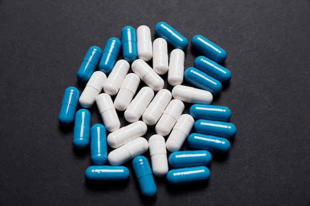 White and blue capsule pills on a black background