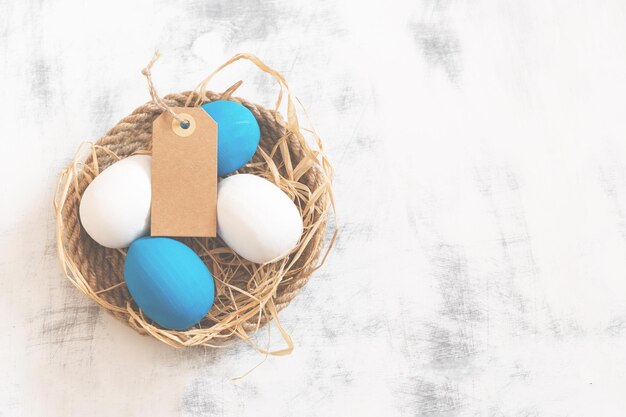 White and blue Easter eggs lie on a tray made of twine under them is hay