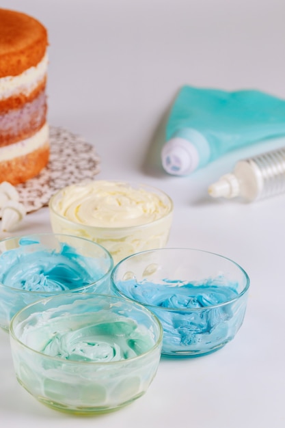 White an blue icing in bowls with round sponge cake befor decoration.
