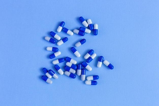 White-and-blue medicine capsules of oval shape lie on a blue background.