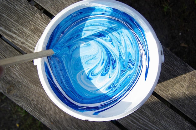 White and blue paint is stirred in a bucket with a stick