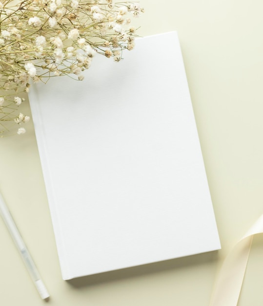 Mockup di copertina vuota per libro bianco su sfondo beige con mockupxa piatto di fiori secchi