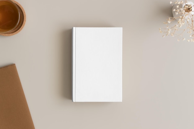 Photo white book mockup with a cup of tea and workspace accessories on a beige table