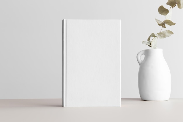 White book mockup with a eucalyptus in a vase on a beige\
table
