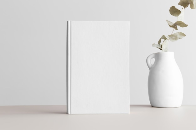 White book mockup with a eucalyptus in a vase on a beige
table