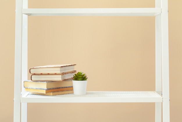 Photo white bookshelf with  books and stationery against beige wall