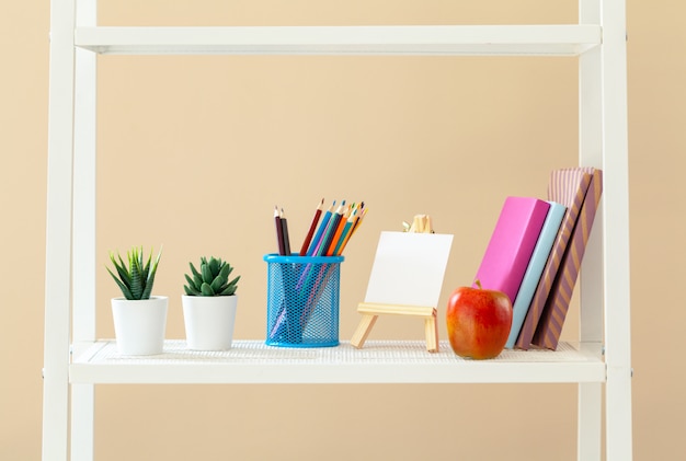 White bookshelf with  books and stationery against beige wall