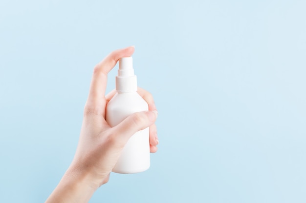 White bottle for antiseptic products with dispenser. Female hand pushing on unbranded plastic container