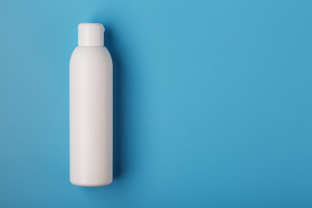 White bottle of cream on a blue background with space for text. Free space for text.