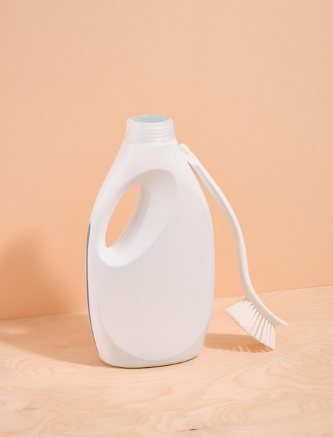 A white bottle of detergent and a white brush with a long handle for cleaning