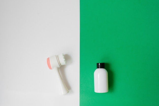 化粧品の白いボトル：シャワージェル、シャンプー、香油またはボディオイル、白と緑の背景に洗顔ブラシ。コピースペース