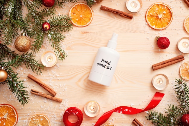 White bottle of hand sanitizer on wooden table with different christmas decorations