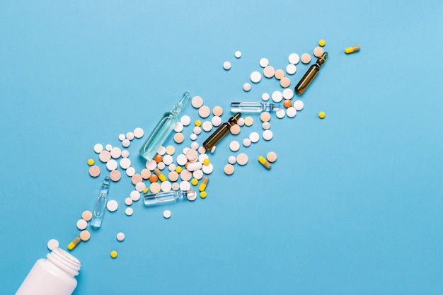 White bottle and multi-colored pills and ampoules with medicines for pricking on a blue background. Concept of pharmaceuticals, medicine, drugs and treatment for diseases. Flat lay, top view