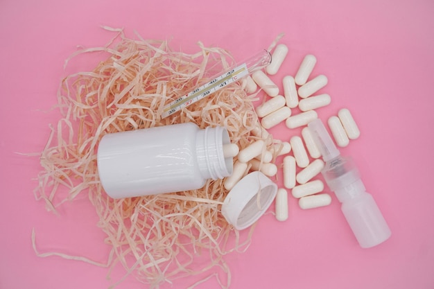 White bottle, nasal spray and thermometer on pink background.